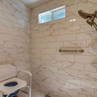 Modern bathroom with marble tiles, featuring a shower head and a safety grab bar.