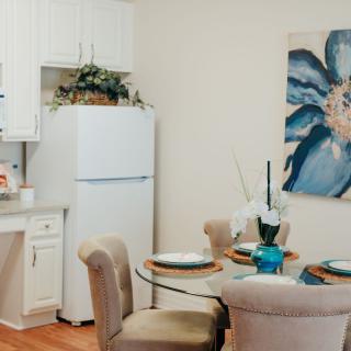 A cozy dining area with a round glass table, set with plates and a centerpiece, and a large floral artwork on the wall.