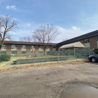 A view of a construction site with a fenced area around a building, set against a cloudy sky.