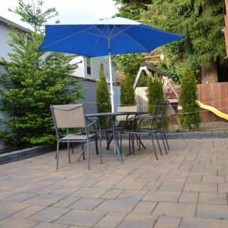 A cozy backyard patio setup with chairs, a table, and a blue umbrella on paving stones.