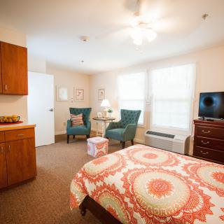 A cozy bedroom with a stylish bedspread, two comfortable chairs, a small round table, and a television near the window.