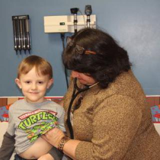 A doctor uses a stethoscope to examine a smiling child during a medical checkup.