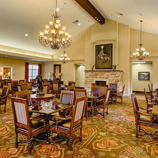 A spacious and elegantly decorated dining room featuring chandeliers, wooden tables and chairs, and a patterned carpet.