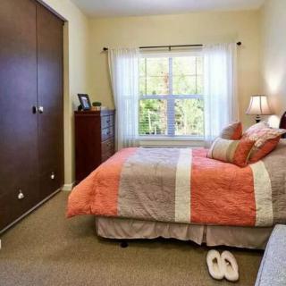 A cozy bedroom with a neatly made bed and colorful bedding, featuring a large window and a wooden closet.