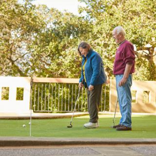 An elderly couple enjoys a game of golf on a sunny day at the putting green.