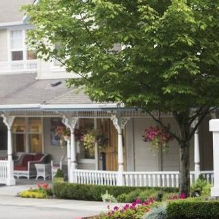 A charming suburban house with a cozy porch adorned with hanging plants and surrounded by trees and flowers.