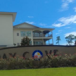 A residential building at Bay Cove, featuring a decorative sign and lush landscaping under a clear blue sky.