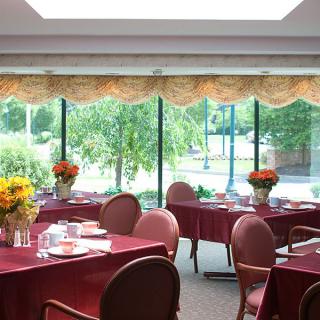A spacious dining area with several tables and chairs, surrounded by large windows allowing natural daylight.