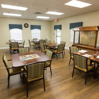 A neatly arranged dining room with multiple tables and chairs, featuring wood flooring and window blinds.