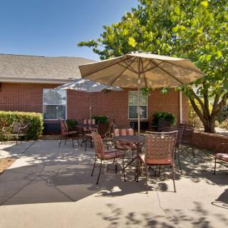 A cozy outdoor patio with tables and chairs under a large umbrella, adjacent to a brick building.