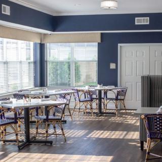 A bright and airy dining area with multiple tables and chairs, illuminated by large windows.