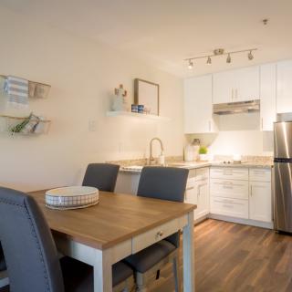 A modern kitchen and dining area with a wooden table, grey chairs, white cabinets, and stainless steel appliances.