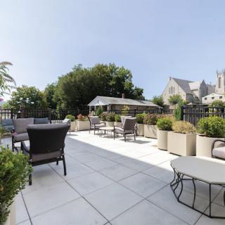 A rooftop terrace with comfortable seating and lush greenery under a clear blue sky.