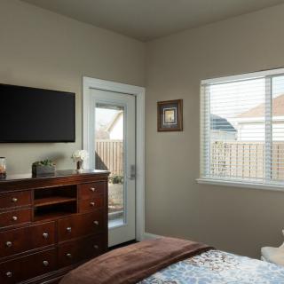 A cozy bedroom with a dresser, wall-mounted television, and a door leading outside.
