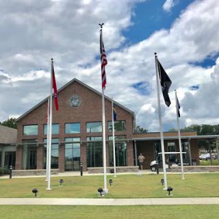 A modern building with multiple flags waving in front, set against a backdrop of a blue sky and fluffy clouds.