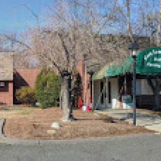 A view of a building featuring a green awning and surrounding landscaping.