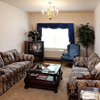 A cozy living room with patterned sofas, a television, and a coffee table under a chandelier.