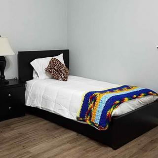 A minimalist bedroom with a single bed, colorful blanket, and a nightstand with a lamp.