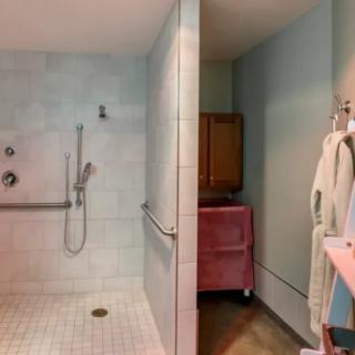 A bathroom with a walk-in shower featuring grab bars and tiled walls, alongside a bathrobe hanging near pastel-colored decor.