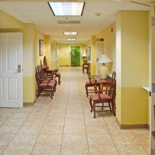 A bright hallway with yellow walls and a tiled floor, featuring chairs arranged in a waiting area.
