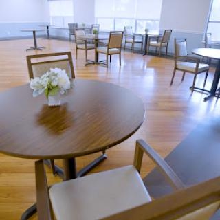 A bright and minimalist dining area featuring wooden tables and chairs, with a small vase of flowers on the table.