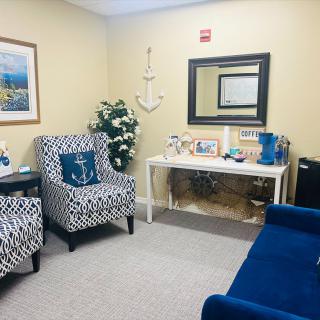 A cozy waiting room with blue and patterned chairs, decorative items, and a mirror on the wall.