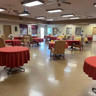 An interior view of a dining area with round tables covered in red tablecloths, arranged for community gatherings.