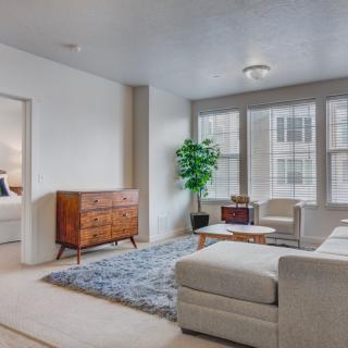 A minimalist living room with a large sofa, wooden furniture, and ample natural light streaming through the windows.