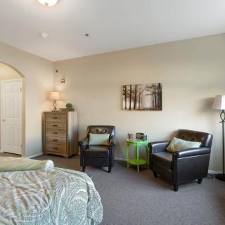A cozy bedroom setup featuring two chairs, a green side table, and a dresser in a well-lit space.