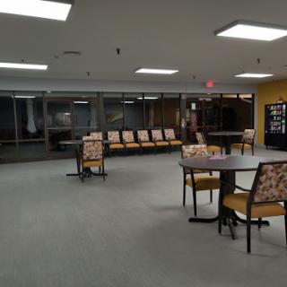 A quiet waiting area with several chairs and tables, illuminated by overhead lights.