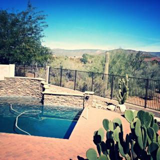 A serene desert landscape featuring a swimming pool with cacti and a distant view of the hills.