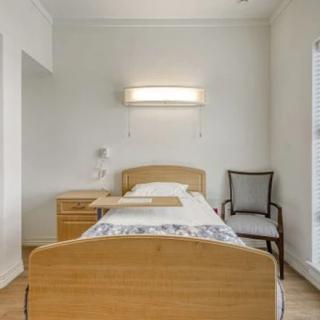 A minimalist bedroom with a single bed, wooden furniture, and a wall lamp.