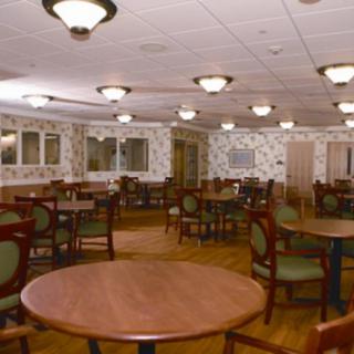 An empty dining room with wooden tables and upholstered chairs, featuring overhead lighting.