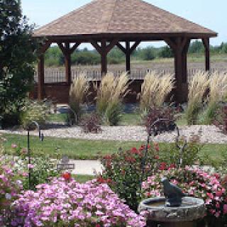 A serene garden featuring a wooden gazebo surrounded by colorful flowers and ornamental grasses.
