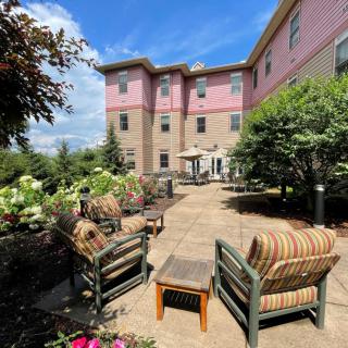 A comfortable outdoor patio area with seating, surrounded by lush greenery and set against a backdrop of a large building.