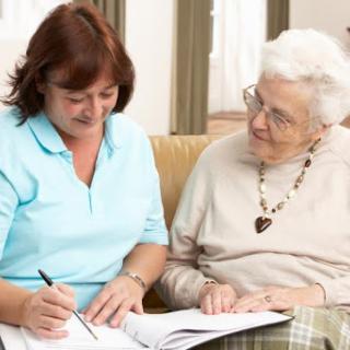 A caregiver and an elderly woman share a moment together, discussing something while writing in a notebook.