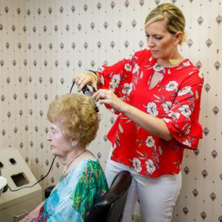 A hairstylist is giving a haircut to an elderly woman in a salon.