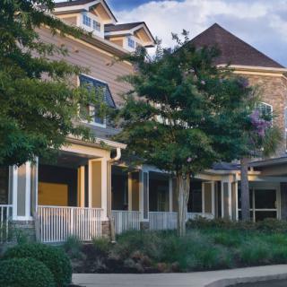 A charming residential house with a welcoming porch and landscaped surroundings.