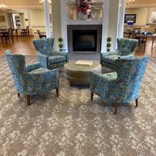 A cozy seating area with patterned chairs arranged around a central ottoman in front of a fireplace.