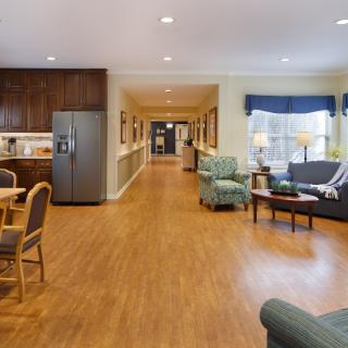 A spacious and well-lit living area with a connected kitchen, featuring cozy seating and wooden flooring.