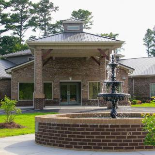 A brick building with a decorative fountain in front and surrounded by greenery.