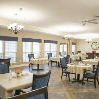 A well-lit dining area with neatly arranged tables and chairs, featuring large windows and overhead lighting.