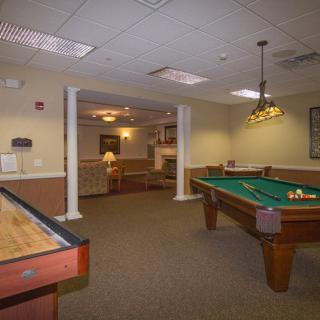 A cozy game room featuring a pool table and shuffleboard under warm indoor lighting.