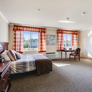 A spacious and well-lit bedroom with a large bed, desk, and two windows with patterned curtains.