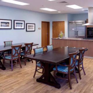 A modern dining area with wooden tables and chairs, adjacent to a kitchen space.