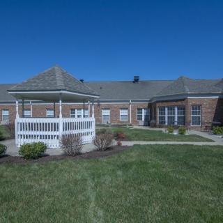A brick building with a white gazebo in front, surrounded by grass under a clear blue sky.