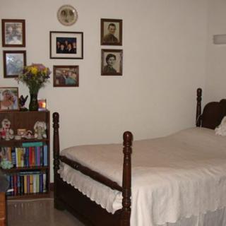 A cozy bedroom with a single bed, decorated with framed photographs and a small bookshelf.