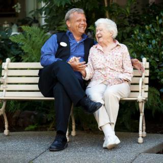 An elderly couple sitting on a bench outdoors, sharing a joyful moment.