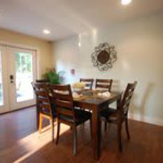 A cozy dining room featuring a wooden dining table with six chairs, complemented by wall art and illuminated by natural light.