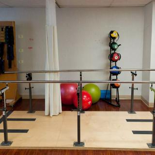 A rehabilitation room equipped with parallel bars and various exercise equipment like medicine balls.